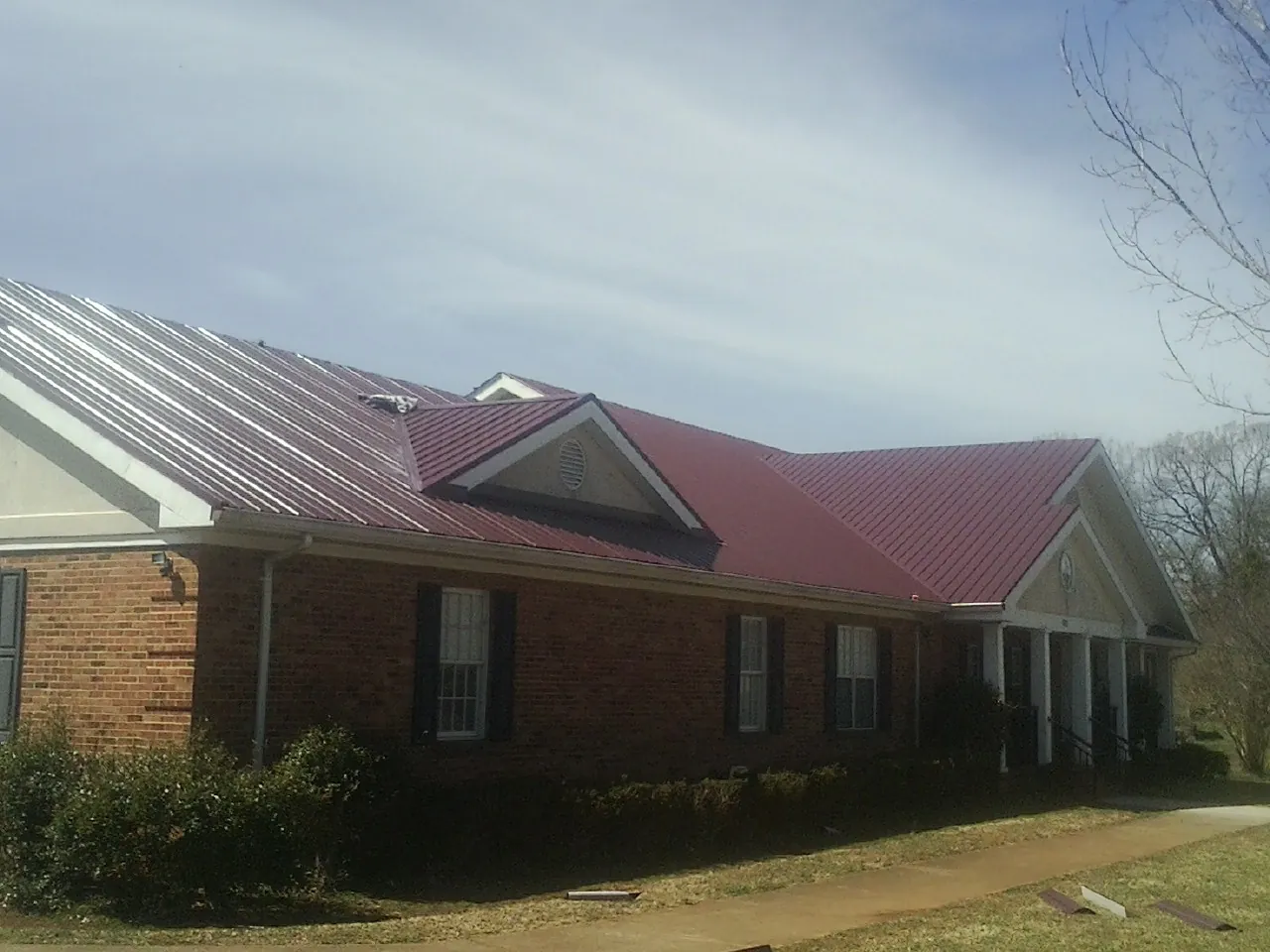 Red metal roof with gabled entries on a long brick building, from a Hail Damage Roof Repair job in Coffeen