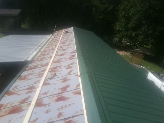 Old rusted panels beside newly installed green metal roofing — Wind Damage Roof Repair by Roofing Brothers in Coffeen