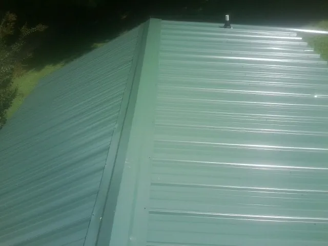 New green metal panels meeting at the ridge of a roof — Flat Roof Repair work by our crew in Coffeen