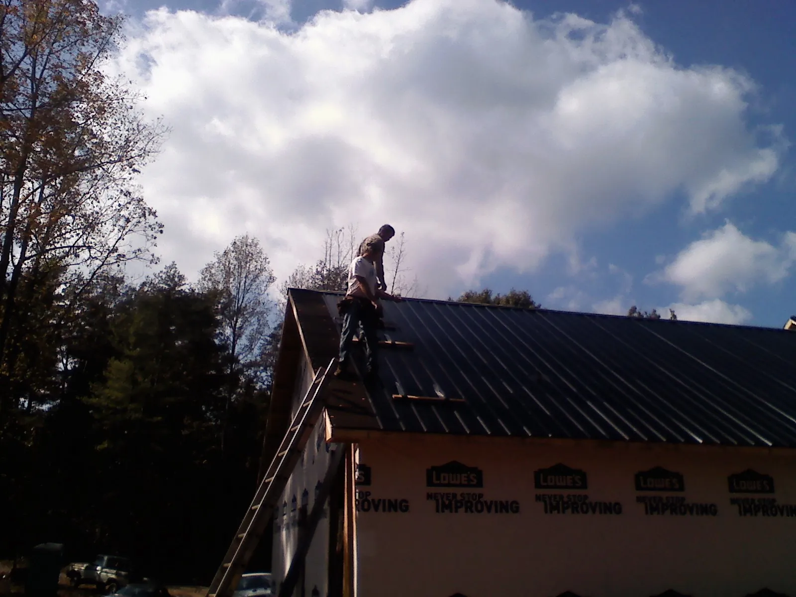 Roofer fastening dark metal panels high against a cloudy sky, from a Roof Inspection job in Coffeen